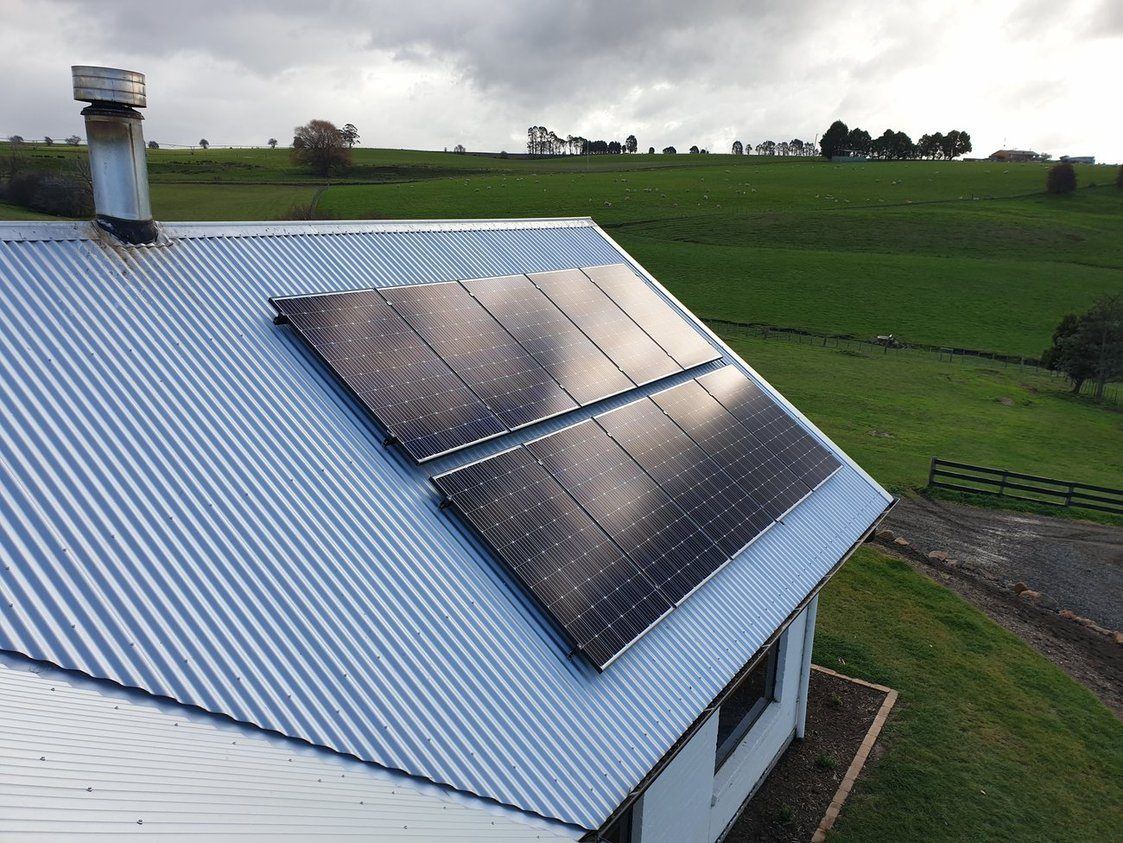 Aerial view of a rooftop solar panel array on a Tasmanian farm shed, with green paddocks behind